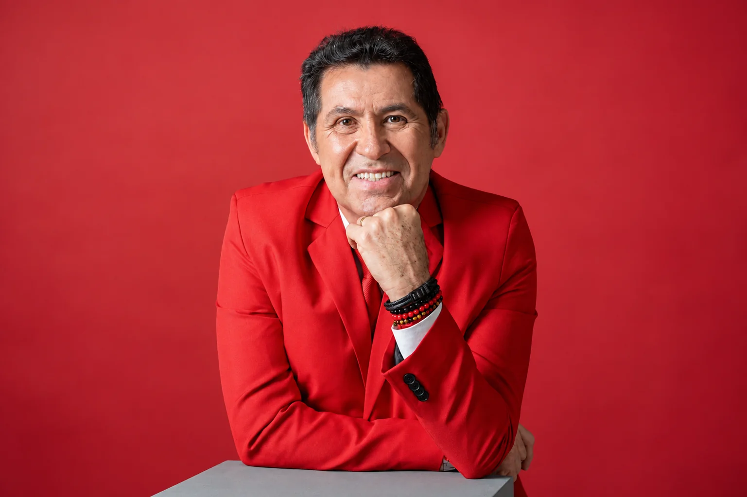 De Assis Diniz de paletó vermelho, mão no queixo, sorrindo